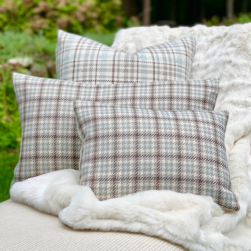 Three differently sized brown, gray and soft blue plaid pillows with a creamy faux fur throw on a chaise.