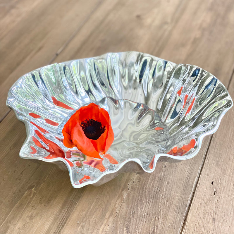 Reflective polished aluminum Vento Medium Bloom Serving Bowl by Beatriz Ball, shown slightly filled with water and a floating orange poppy.