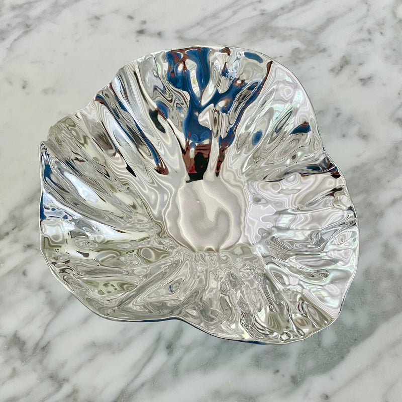The polished aluminum Vento Small Bloom Bowl by Beatriz Ball, features a rippled and wavy edge. Shown here from the top on a marble counter.