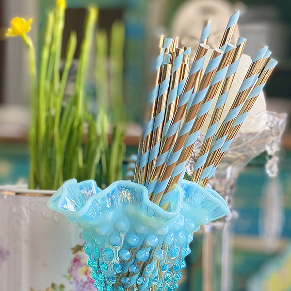 Vintage vase filled with light blue and metallic gold striped paper party straws.