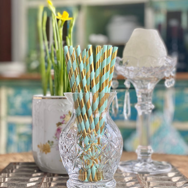 Crystal vase holding mint and metallic gold striped paper party straws.