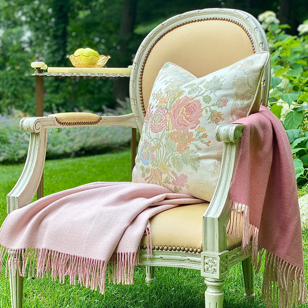The Vita white and floral pillow on a butterscotch  leather sheild back chair with pink throuw outside.