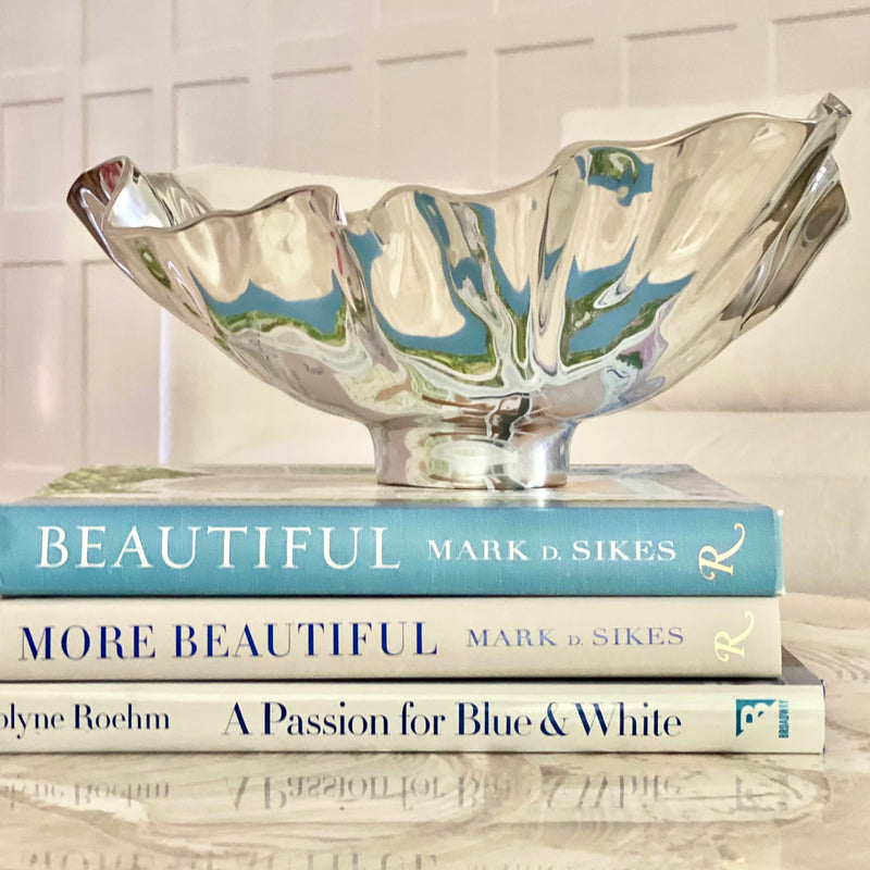 Stunning polished aluminum Vento Medium Bloom bowl by Beatriz Ball, featuring an organic rippled edge. Shown resting atop a stack of design books.